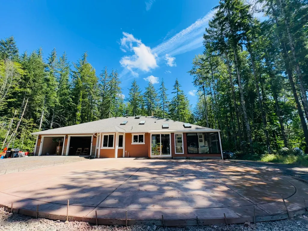 Large colored concrete driveway with curved edge forms still in place in front of a home surrounded by evergreens
