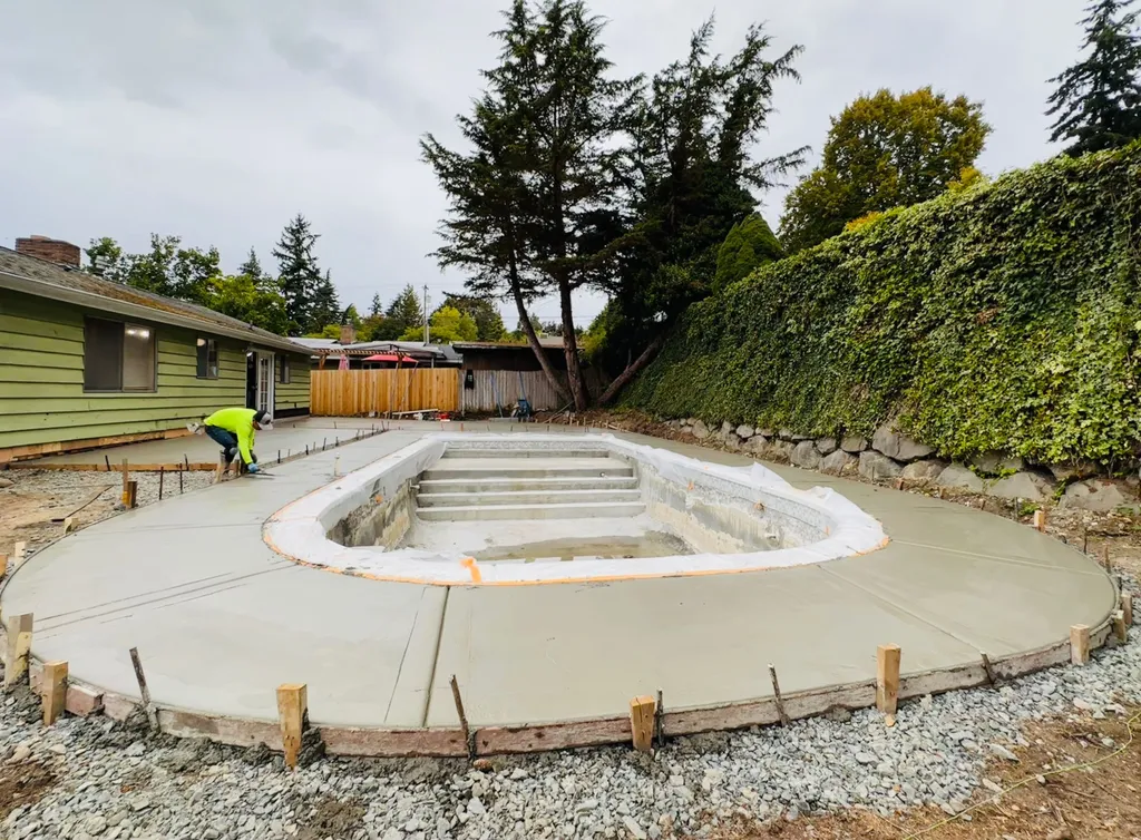 Freshly poured concrete pool deck around an inground pool while a finisher works the far edge