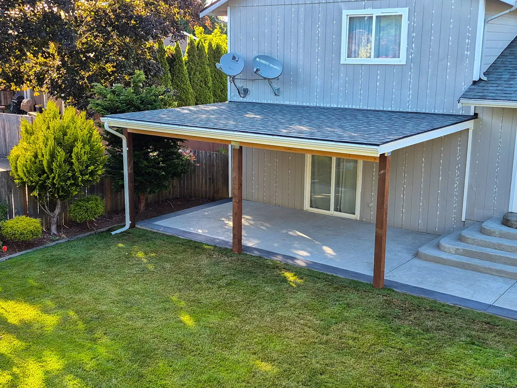 Finished covered patio with a shingled roof and wood posts over a stamped concrete slab with curved steps