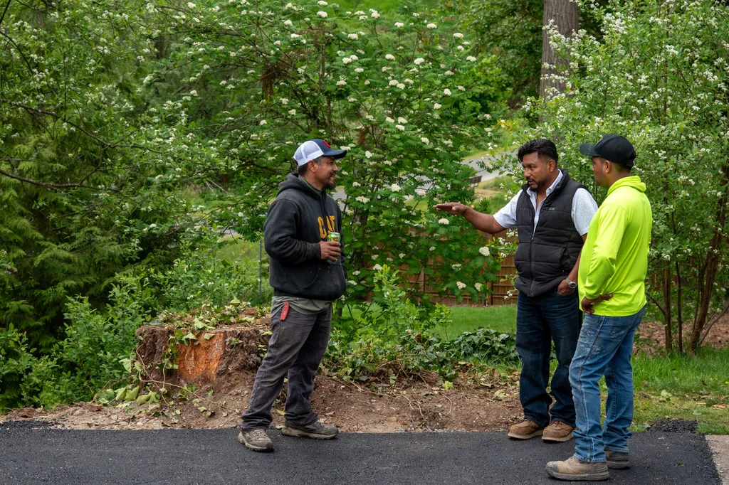 Three crew members talking through a plan at the edge of a newly paved asphalt driveway